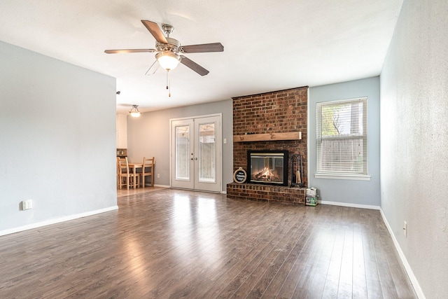 unfurnished living room with baseboards, french doors, a ceiling fan, a brick fireplace, and wood finished floors