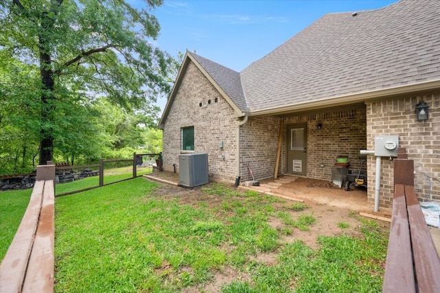 back of property featuring brick siding, a yard, a shingled roof, and central AC unit