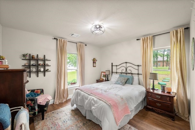 bedroom with wood finished floors, visible vents, and multiple windows