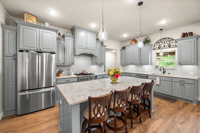 kitchen with appliances with stainless steel finishes, backsplash, a sink, gray cabinetry, and a center island