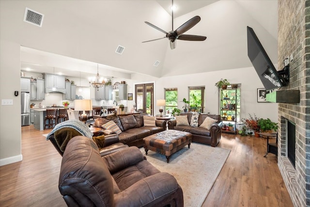 living room with visible vents, ceiling fan with notable chandelier, a brick fireplace, and high vaulted ceiling