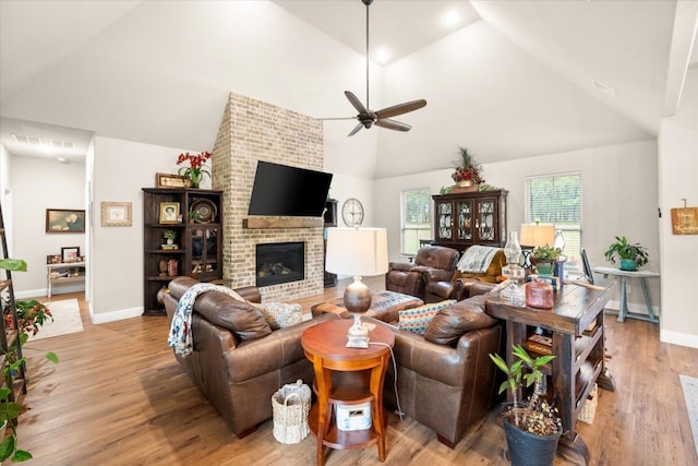 living room with a fireplace, high vaulted ceiling, a ceiling fan, light wood-style flooring, and baseboards