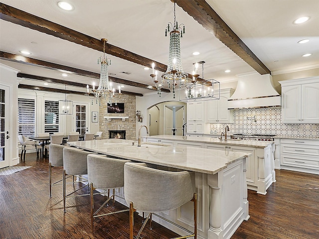 kitchen with a spacious island, a notable chandelier, custom range hood, a fireplace, and dark wood-type flooring