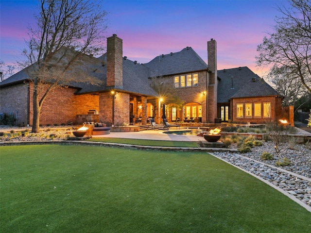 back of house at dusk featuring a chimney, brick siding, an outdoor pool, and a patio area