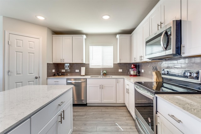 kitchen with white cabinets, a sink, light wood finished floors, stainless steel appliances, and tasteful backsplash