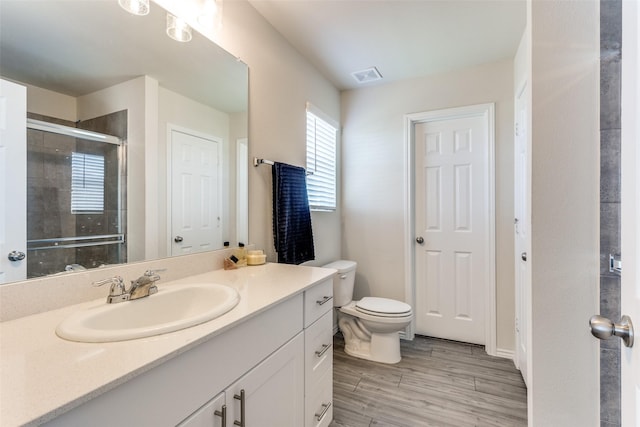 bathroom with visible vents, a shower stall, wood finished floors, vanity, and toilet