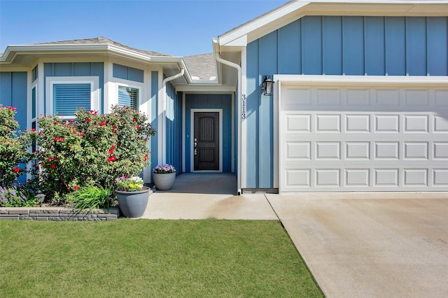 doorway to property with a shingled roof, a garage, board and batten siding, concrete driveway, and a lawn