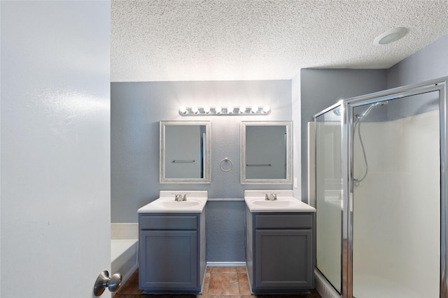 bathroom featuring a sink, two vanities, a stall shower, and a textured ceiling