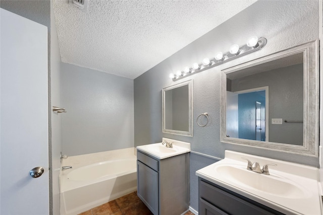 full bath with two vanities, a bath, a textured ceiling, tile patterned flooring, and a sink