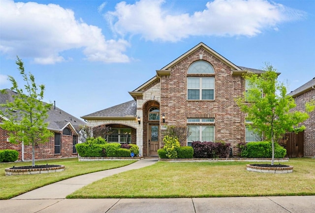 traditional-style house featuring a front yard, fence, and brick siding