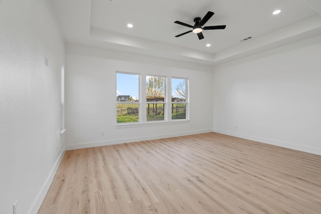 empty room featuring baseboards, recessed lighting, light wood-style floors, a tray ceiling, and ceiling fan