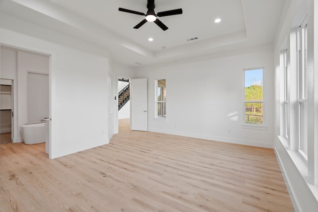 interior space featuring a tray ceiling, light wood finished floors, and baseboards