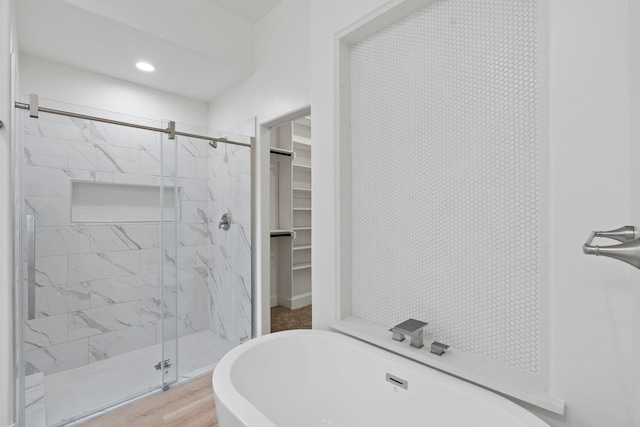 full bathroom featuring a walk in closet, a freestanding bath, a shower stall, and wood finished floors
