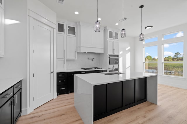 kitchen with tasteful backsplash, gas cooktop, a sink, a center island with sink, and light wood finished floors
