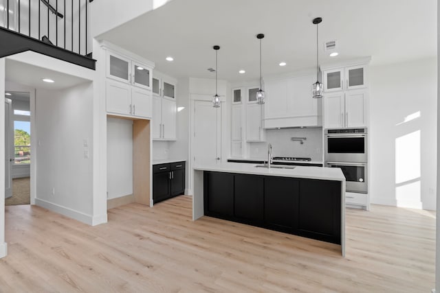 kitchen with light countertops, white cabinetry, stainless steel double oven, visible vents, and a sink