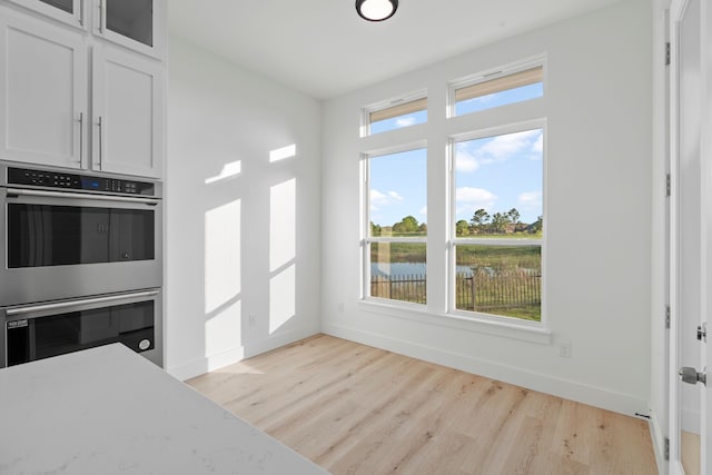kitchen featuring glass insert cabinets, white cabinets, baseboards, double oven, and light wood-style flooring