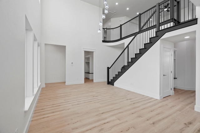 unfurnished living room featuring a towering ceiling, wood finished floors, baseboards, and stairway