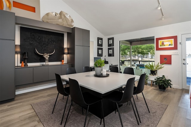dining space with light wood-type flooring, rail lighting, and lofted ceiling