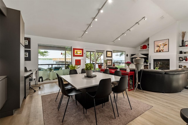 dining area with rail lighting, lofted ceiling, a glass covered fireplace, and light wood-style flooring