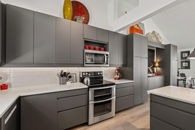 kitchen featuring backsplash, vaulted ceiling, gray cabinets, and stainless steel appliances
