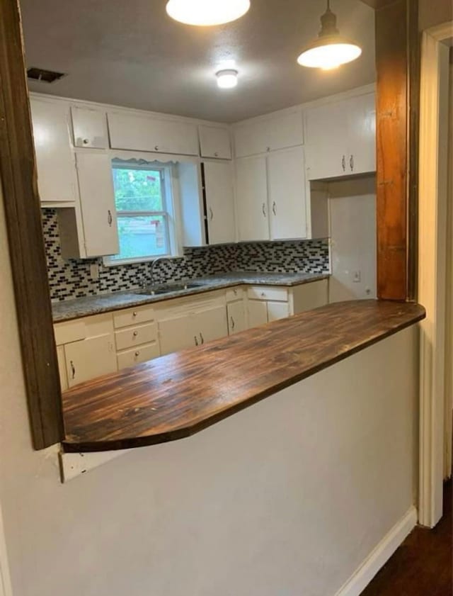 kitchen with white cabinetry, dark wood-style flooring, a sink, wood counters, and decorative backsplash