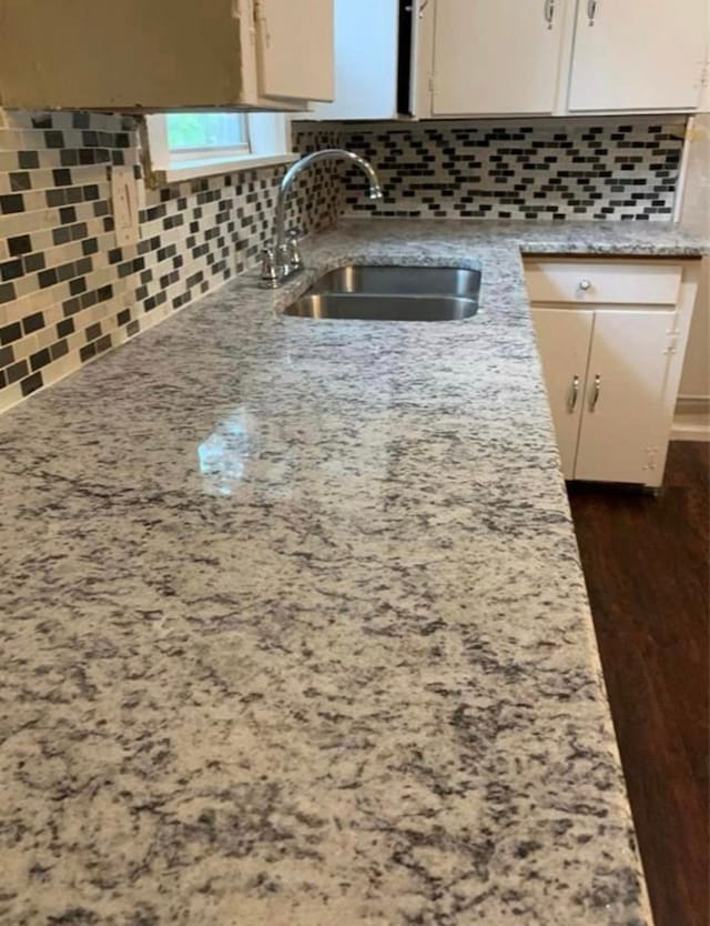 kitchen with a sink, light stone counters, and decorative backsplash