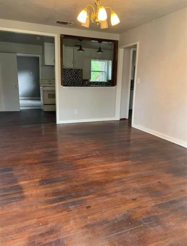 empty room with visible vents, a notable chandelier, dark wood finished floors, and baseboards