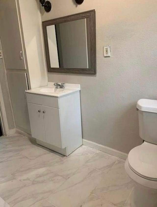 half bath featuring toilet, marble finish floor, baseboards, and vanity
