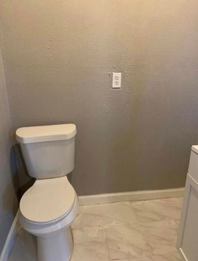 bathroom with toilet, marble finish floor, and baseboards