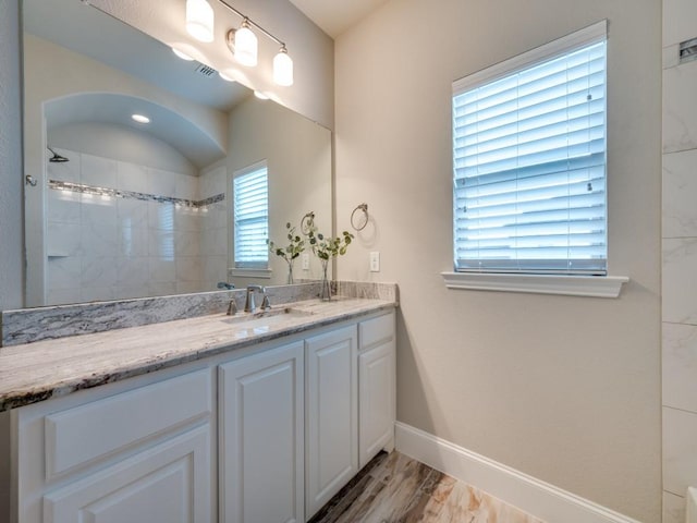 full bathroom featuring vanity, visible vents, wood finished floors, baseboards, and tiled shower