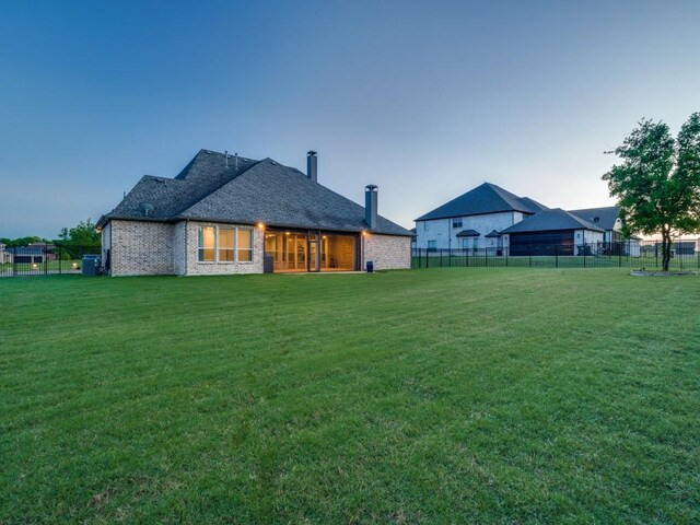 back of house at dusk featuring a lawn, a fenced backyard, and brick siding