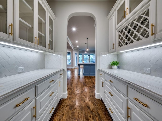 bar with arched walkways, dark wood-style floors, decorative backsplash, and recessed lighting