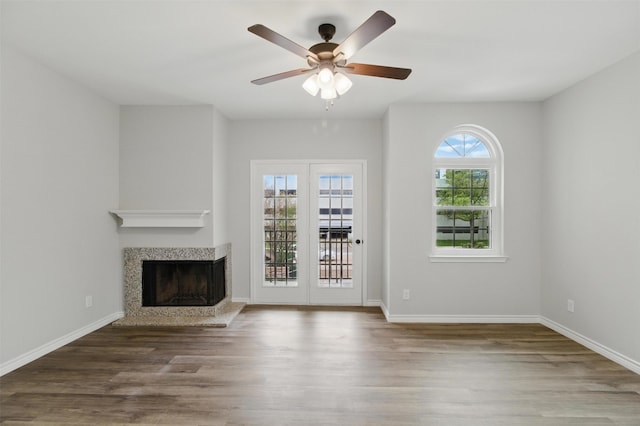 unfurnished living room with wood finished floors, a ceiling fan, a multi sided fireplace, and baseboards