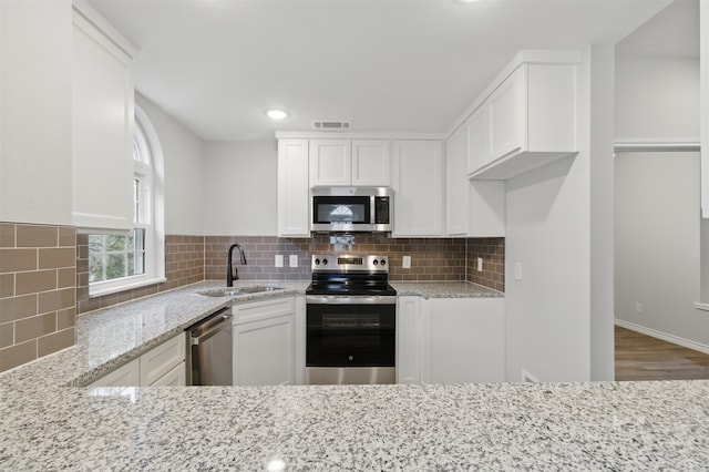 kitchen featuring white cabinetry, light stone countertops, appliances with stainless steel finishes, and a sink