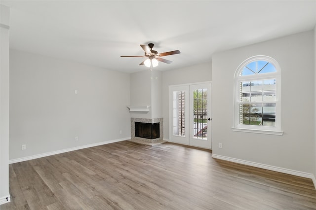unfurnished living room featuring a fireplace, wood finished floors, ceiling fan, and baseboards