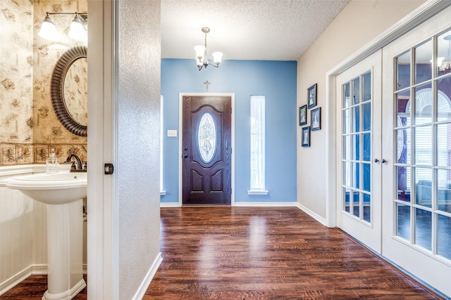 entryway with a notable chandelier, wood finished floors, baseboards, a textured ceiling, and french doors