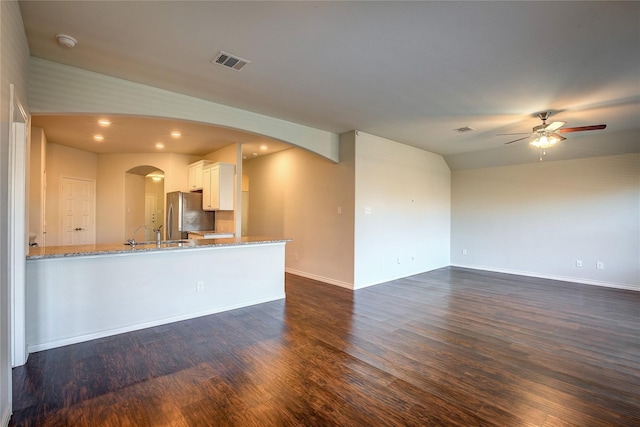 unfurnished living room with dark wood finished floors, ceiling fan, arched walkways, and visible vents