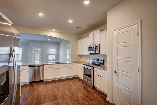 kitchen with dark wood-style floors, light stone counters, stainless steel appliances, arched walkways, and white cabinetry