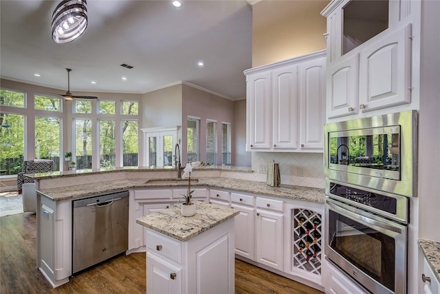 kitchen with tasteful backsplash, ornamental molding, a peninsula, stainless steel appliances, and a sink