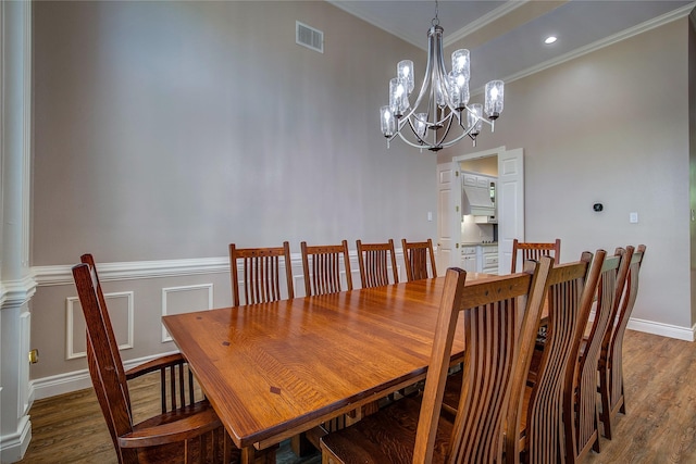 dining space featuring a notable chandelier, crown molding, wainscoting, visible vents, and wood finished floors