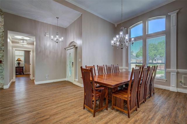dining area with a notable chandelier, baseboards, ornamental molding, a high ceiling, and wood finished floors