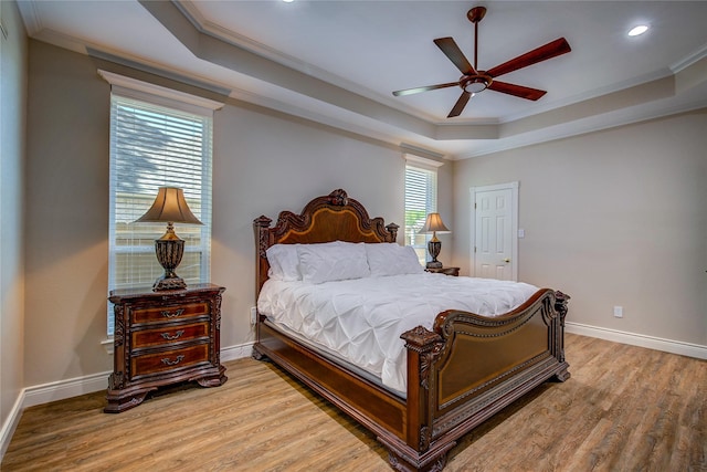 bedroom with baseboards, recessed lighting, crown molding, a raised ceiling, and wood finished floors