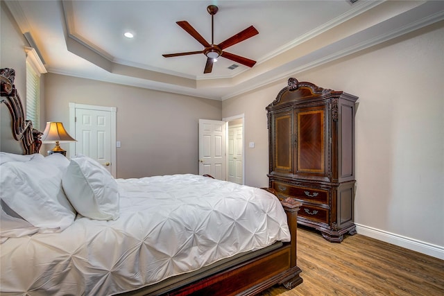 bedroom featuring crown molding, ceiling fan, a tray ceiling, wood finished floors, and baseboards