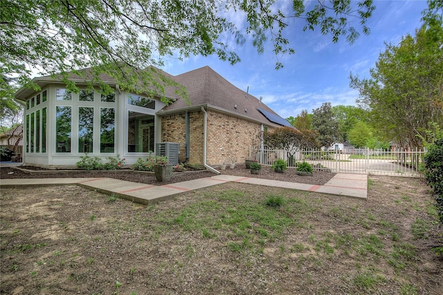 rear view of property with a gate, brick siding, central AC, fence, and a shingled roof