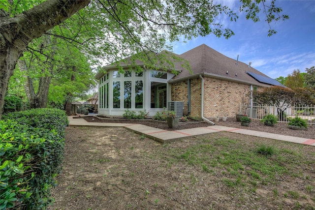 back of property featuring cooling unit, roof with shingles, fence, and brick siding