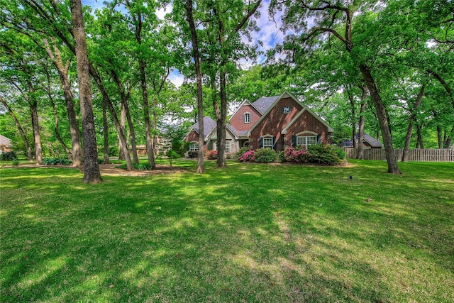tudor-style house featuring brick siding, fence, and a front yard