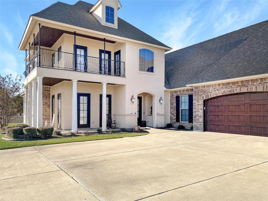 view of front of home with concrete driveway, a balcony, stucco siding, brick siding, and a shingled roof