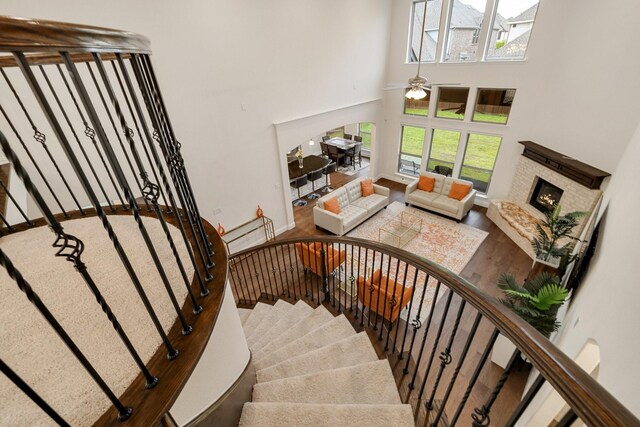14662 Gentle Breeze Rd, Frisco, TX 75035 - stairs with ceiling fan, a lit fireplace, a towering ceiling, wood finished floors, and baseboards