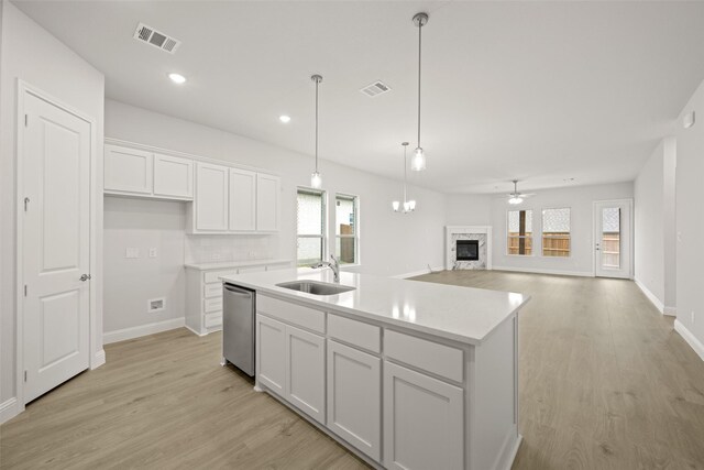 2297 High Plain Ln, Waxahachie, TX 75167 - kitchen with stainless steel dishwasher, a sink, a stone fireplace, white cabinetry, and light wood-type flooring