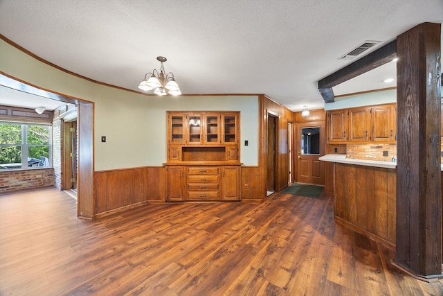kitchen featuring brown cabinetry, dark wood-type flooring, visible vents, and a wainscoted wall